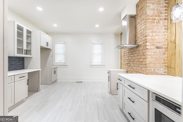 kitchen with white cabinets, wall chimney range hood, tasteful backsplash, and stainless steel microwave