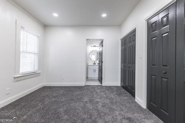 unfurnished bedroom featuring ensuite bath, dark colored carpet, and sink