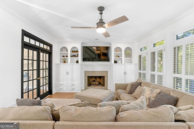 living room featuring built in shelves, ceiling fan, wood-type flooring, and ornamental molding