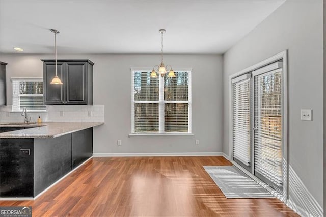 kitchen featuring decorative light fixtures, backsplash, sink, an inviting chandelier, and light stone countertops