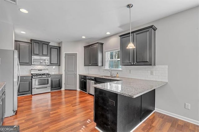 kitchen with stainless steel appliances, pendant lighting, light hardwood / wood-style flooring, light stone counters, and sink