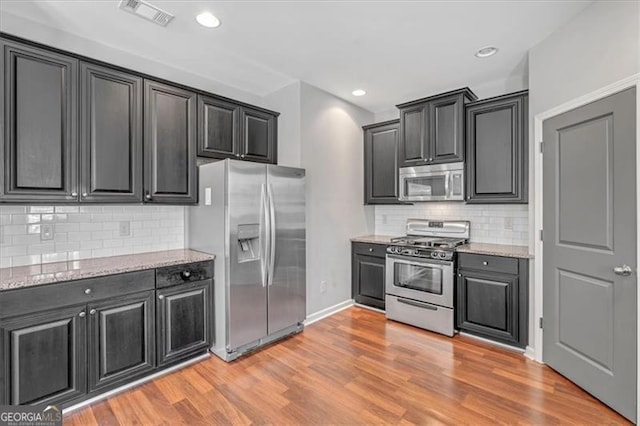 kitchen with light wood-type flooring, stainless steel appliances, decorative backsplash, and light stone counters