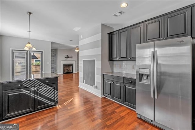 kitchen featuring pendant lighting, stainless steel refrigerator with ice dispenser, dark wood-type flooring, dark stone counters, and backsplash