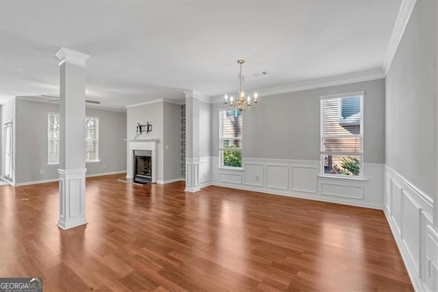 unfurnished living room with hardwood / wood-style floors, a notable chandelier, crown molding, and decorative columns