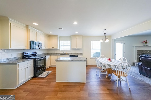 kitchen with black appliances, hanging light fixtures, hardwood / wood-style floors, and light stone counters