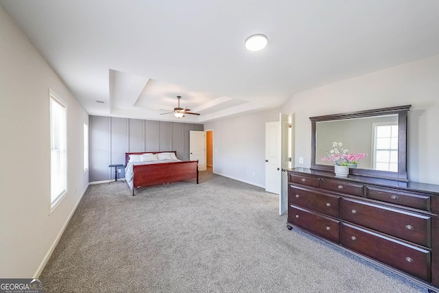 bedroom with ceiling fan, a tray ceiling, light carpet, and multiple windows