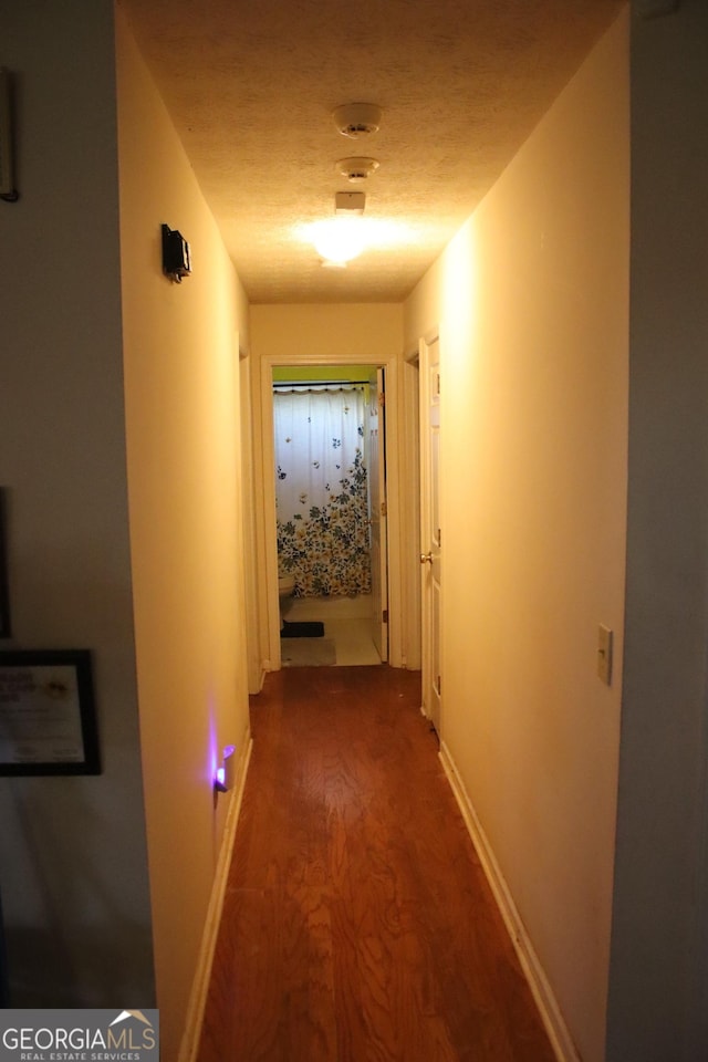 hallway with a textured ceiling and dark wood-type flooring