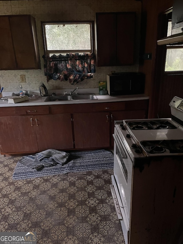 kitchen featuring sink, decorative backsplash, white gas stove, and dark brown cabinetry