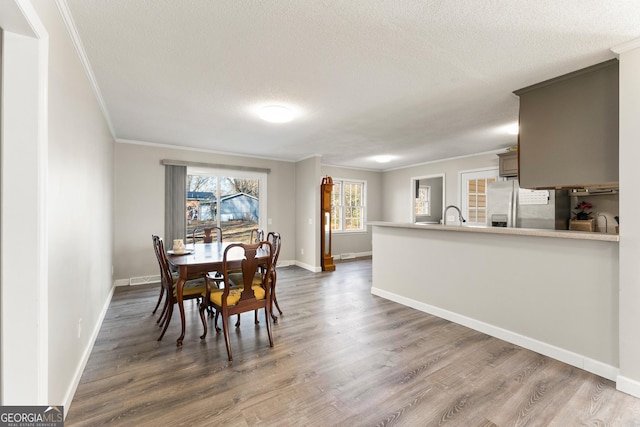 dining room with sink, a textured ceiling, ornamental molding, and dark hardwood / wood-style floors