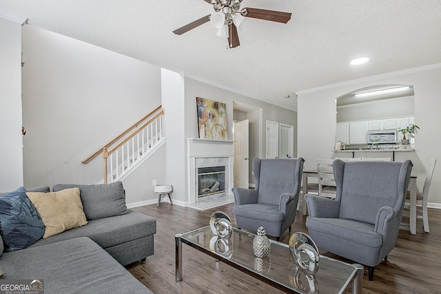 living room featuring hardwood / wood-style floors, a high end fireplace, ornamental molding, ceiling fan, and a textured ceiling