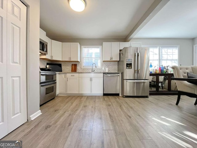 kitchen featuring a healthy amount of sunlight, stainless steel appliances, white cabinetry, and backsplash