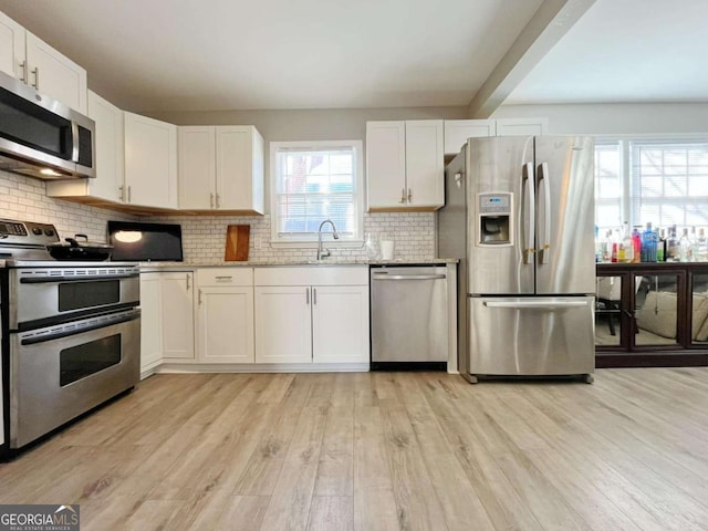 kitchen featuring stainless steel appliances, light hardwood / wood-style floors, decorative backsplash, white cabinetry, and sink