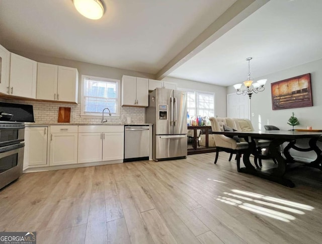 kitchen featuring tasteful backsplash, an inviting chandelier, light wood-type flooring, white cabinets, and appliances with stainless steel finishes