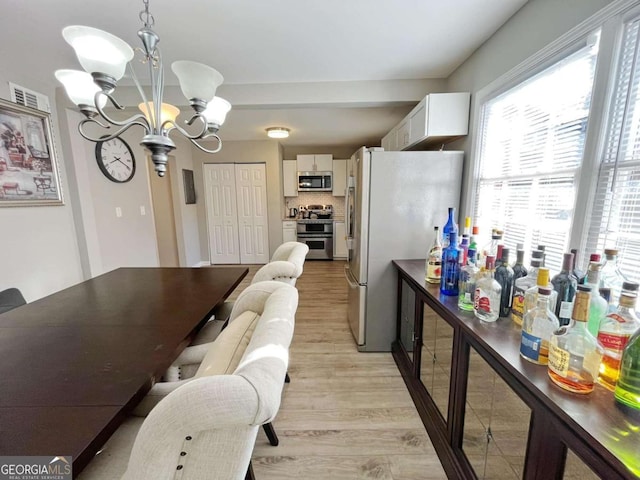 kitchen featuring stainless steel appliances, white cabinets, decorative light fixtures, light hardwood / wood-style flooring, and a notable chandelier