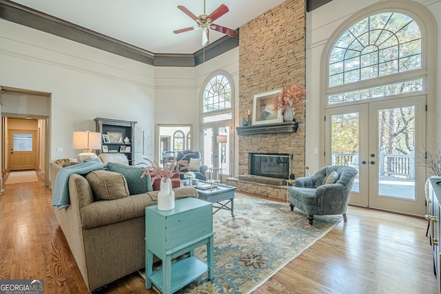 living room featuring french doors, a stone fireplace, a high ceiling, and wood finished floors