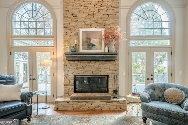 living area featuring french doors, a stone fireplace, and a high ceiling