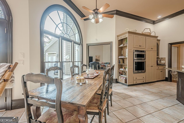 dining room featuring crown molding, light tile patterned floors, a towering ceiling, ceiling fan, and baseboards