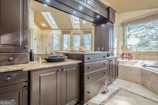 kitchen with dark brown cabinetry, lofted ceiling with skylight, light stone counters, a sink, and light tile patterned flooring