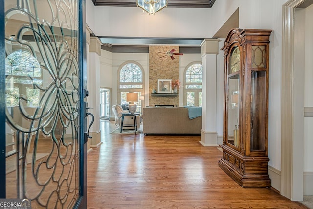 foyer with a stone fireplace, crown molding, a high ceiling, wood finished floors, and ornate columns