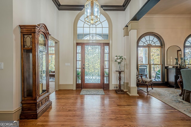 foyer with a high ceiling, wood finished floors, baseboards, ornamental molding, and an inviting chandelier