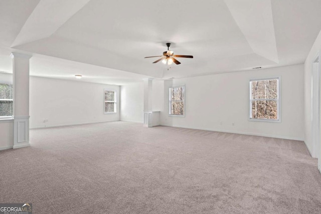 empty room featuring light colored carpet, ceiling fan, a tray ceiling, and a healthy amount of sunlight