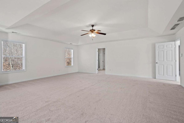 empty room featuring ceiling fan, light colored carpet, and a tray ceiling