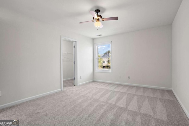 unfurnished bedroom with ceiling fan, a spacious closet, a closet, and light carpet