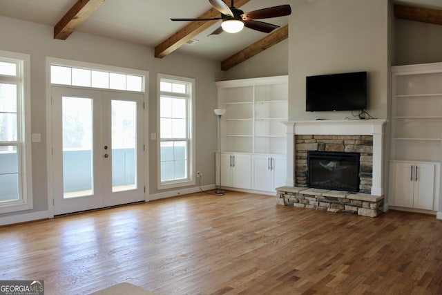 unfurnished living room with light wood-type flooring, beamed ceiling, ceiling fan, french doors, and a fireplace