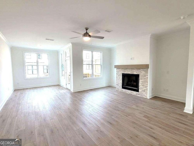 unfurnished living room with crown molding, ceiling fan, plenty of natural light, and a stone fireplace