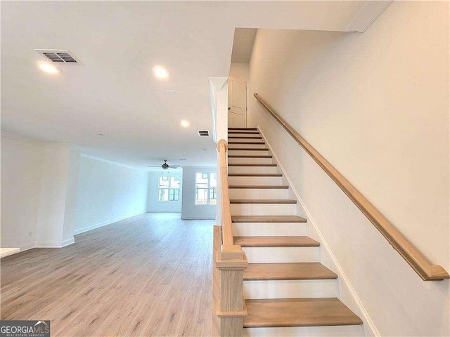 stairway featuring ceiling fan, ornamental molding, and wood-type flooring