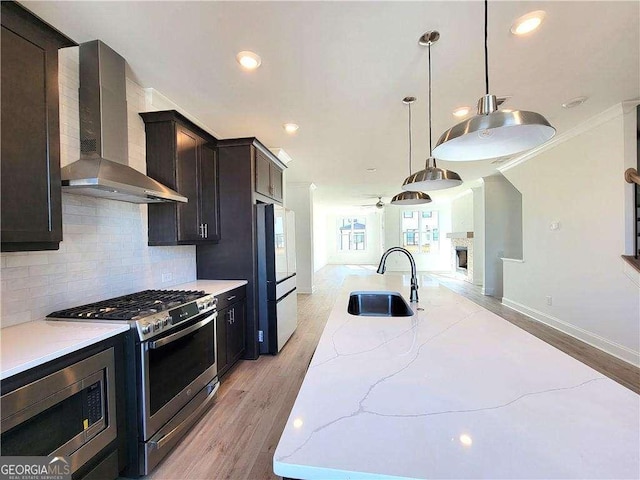 kitchen with stainless steel appliances, decorative light fixtures, wall chimney range hood, light stone counters, and sink