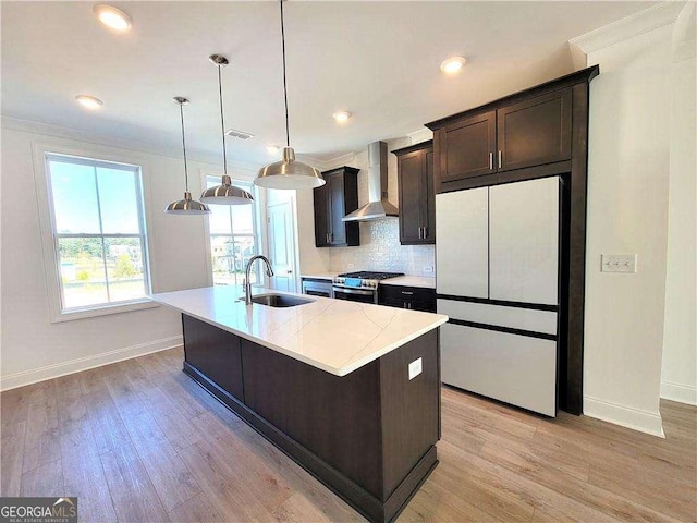 kitchen with gas stove, a kitchen island with sink, wall chimney range hood, white refrigerator, and sink