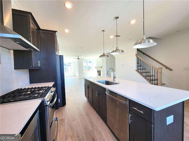 kitchen featuring wall chimney exhaust hood, stainless steel appliances, sink, hanging light fixtures, and a large island