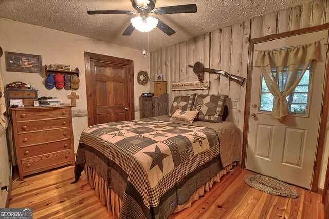 bedroom with wooden walls, a textured ceiling, ceiling fan, and light hardwood / wood-style floors