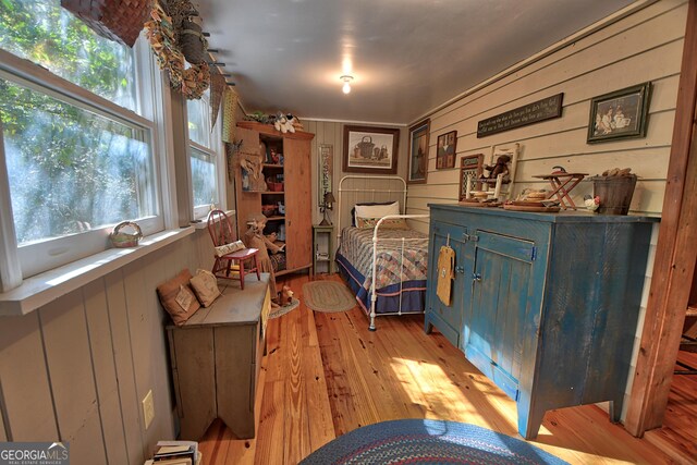 bedroom featuring wood walls, light hardwood / wood-style flooring, and multiple windows