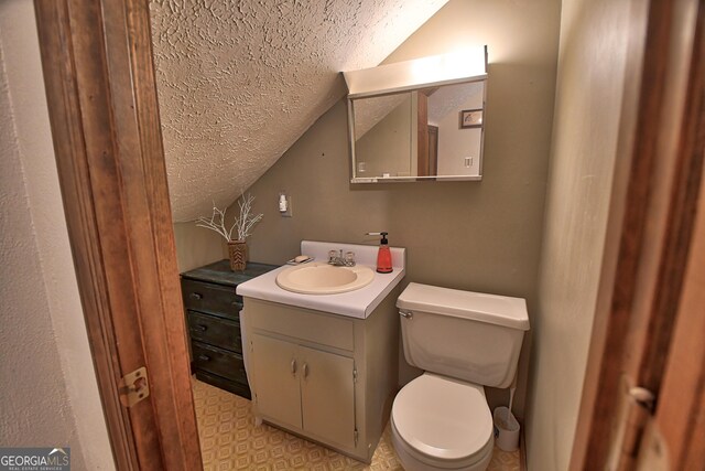 bathroom with lofted ceiling, a textured ceiling, toilet, and vanity