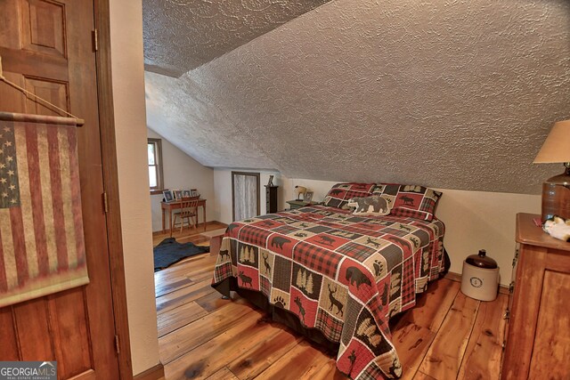 bedroom featuring a textured ceiling, vaulted ceiling, and hardwood / wood-style floors