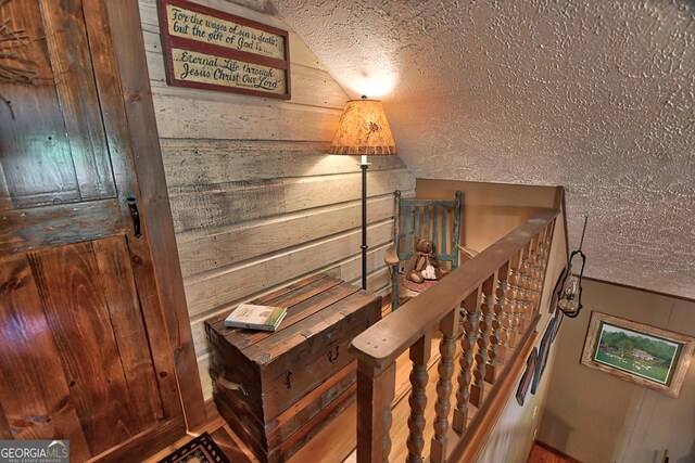 stairway featuring lofted ceiling, a textured ceiling, and wood walls