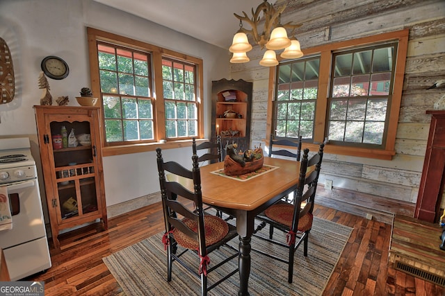 dining room with dark wood-type flooring, an inviting chandelier, and wooden walls