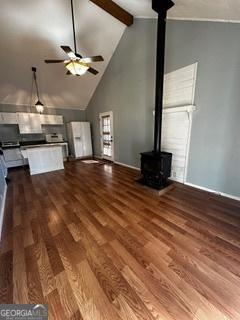 unfurnished living room featuring wood-type flooring, beamed ceiling, ceiling fan, high vaulted ceiling, and a wood stove