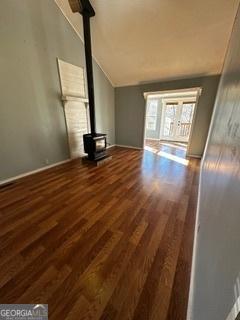 unfurnished living room featuring lofted ceiling, a wood stove, and dark wood-type flooring