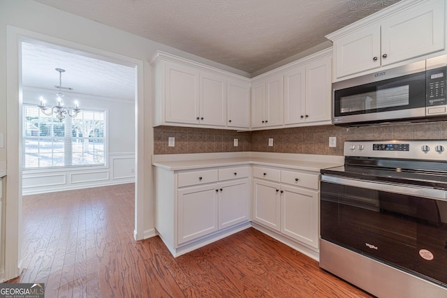 kitchen featuring an inviting chandelier, appliances with stainless steel finishes, wood-type flooring, and white cabinetry