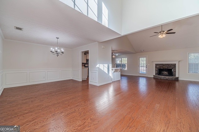 unfurnished living room with high vaulted ceiling, a stone fireplace, ceiling fan with notable chandelier, and hardwood / wood-style floors