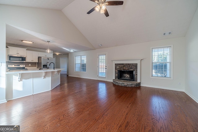 unfurnished living room with ceiling fan, dark hardwood / wood-style flooring, a stone fireplace, and lofted ceiling