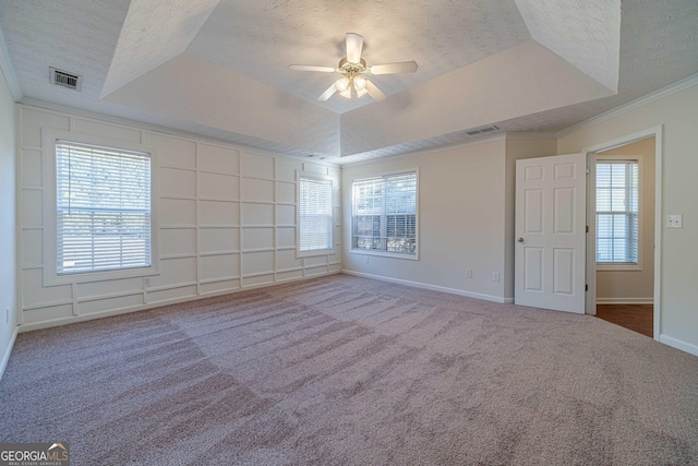 carpeted empty room with ceiling fan, a wealth of natural light, crown molding, and a raised ceiling