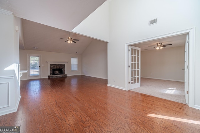 unfurnished living room with high vaulted ceiling, hardwood / wood-style floors, a stone fireplace, and french doors