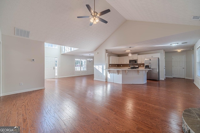 unfurnished living room with ceiling fan with notable chandelier, a textured ceiling, dark hardwood / wood-style flooring, and high vaulted ceiling