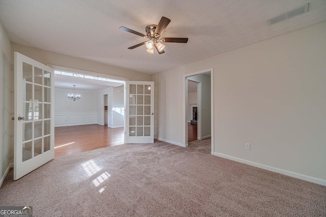 carpeted spare room with a textured ceiling, ceiling fan with notable chandelier, and french doors