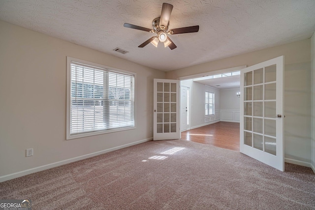 carpeted empty room featuring ceiling fan, french doors, and a wealth of natural light