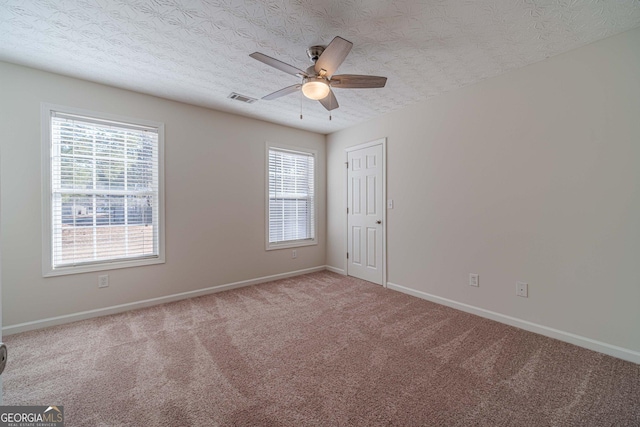 carpeted empty room with ceiling fan, plenty of natural light, and a textured ceiling